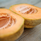 Two halves of a ripe Amish melon cantaloupe showing orange flesh and seeds on a wooden surface.
