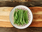 Freshly harvested Blue Lake FM1K pole beans in a decorative white bowl on a rustic wooden cutting board.