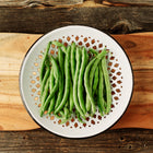 Freshly harvested Blue Lake FM1K pole beans in a decorative white bowl on a rustic wooden cutting board.