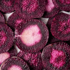 Close-up of sliced Black Nebula carrot rounds showing deep purple-black skin and vibrant magenta-purple flesh.