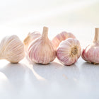 Several Chesnok Red garlic bulbs with purple-striped papery skins arranged on a white surface.