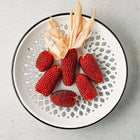 Small, deep red Strawberry Popcorn ears arranged on a white decorative plate with a black rim.