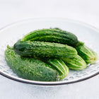 Fresh A & C Pickling cucumbers in a white metal colander against a light background.