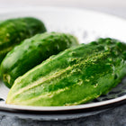 Three fresh, bumpy Bushy cucumbers resting in a white decorative bowl.