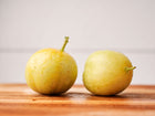 Two round, pale yellow Lemon cucumber fruits resting on a wooden surface against a white background.