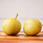 Two round, pale yellow Lemon cucumber fruits resting on a wooden surface against a white background.