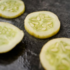 Thinly sliced yellow Lemon cucumber rounds with visible seeds resting on a dark, textured surface.
