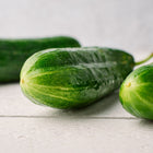 Three fresh, smooth-skinned Muncher cucumbers resting on a white wooden surface.