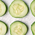 Six fresh, sliced Muncher cucumber rounds arranged in rows on a white textured surface.