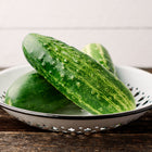 Fresh Spacemaster 80 cucumbers in a white metal colander on a rustic wooden table.