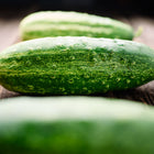 Three dark green Spacemaster 80 cucumbers resting on a rustic wooden surface.