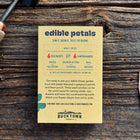 Edible Petals seed kit box with six seed packets and birch garden markers on a rustic wooden surface.