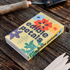 Edible Petals seed kit in a yellow matchbox-style package with floral illustrations on a rustic wooden table with garden markers.