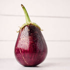Glossy, deep purple Black Beauty eggplant with water droplets against a white wooden background.