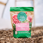 Gaia Green Power Bloom 2-8-4 fertilizer bag standing on soil in a greenhouse.