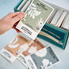 Hand holding a Holy Tulsi Basil seed packet above a box of assorted seed packets.