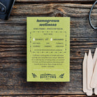 Green Homegrown Wellness seed kit box on a rustic wooden surface with garden tools and wooden plant markers.