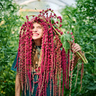 Smiling person holding a large bunch of deep crimson Love-Lies-Bleeding amaranth tassels over their head in a garden.