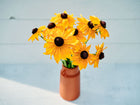 Bouquet of golden-orange Marmalade rudbeckia flowers with dark centers in a terracotta vase on a white surface.