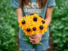 Person holding a fresh bouquet of golden-orange Marmalade rudbeckia flowers with dark centers in a garden.