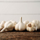 Several Music garlic bulbs with white papery skins arranged on a rustic dark wooden surface.