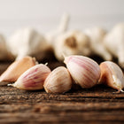 Music garlic cloves with blush-pink skins resting on a rustic wooden surface with whole bulbs blurred in the background.