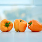 Three vibrant, blocky Orange Sun sweet peppers with green stems sitting on a light surface.
