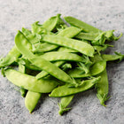 A pile of fresh, bright green Oregon Sugar Pod II snow pea pods on a textured gray surface.