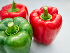 Fresh California Wonder bell peppers in red and green with water droplets on a light surface.