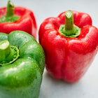 Fresh California Wonder bell peppers in red and green with water droplets on a light surface.