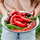 Person holding a white enamel bowl filled with freshly harvested red and green Hot Portugal peppers.