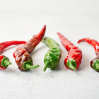 Five long, slender Hot Portugal peppers in varying stages of red and green ripeness on a white surface.