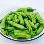 Fresh green Shishito peppers piled in a white enameled metal colander with a black rim.