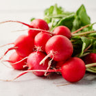 A bunch of freshly harvested, round, bright red Cherry Belle radishes with green leafy tops on a white surface.