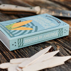 Rooted in America seed kit box with corn illustration and white birch garden markers on a rustic wooden surface.