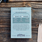 Rooted in America seed kit box with six seed varieties listed, next to white birch garden markers on a wooden surface.