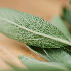 Close-up of textured, gray-green Broadleaf sage leaves resting on a wooden surface.