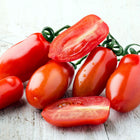 Freshly harvested red San Marzano tomatoes, some whole and some sliced, on a rustic white wooden surface.