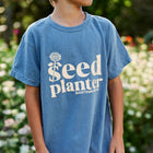 Person wearing a blue garment-dyed Seed Planter short sleeve cotton t-shirt with a white flower graphic.