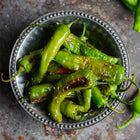 Blistered green Shishito peppers seasoned with salt in a decorative metal bowl on a dark textured surface.
