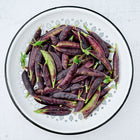 Freshly harvested Sugar Magnolia snap peas with deep purple pods in a white patterned colander.