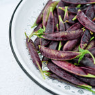 Freshly harvested Sugar Magnolia snap peas with deep purple pods in a white metal colander.
