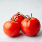 Three bright red Ace 55 tomatoes on a vine resting on a light, textured surface.