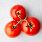 Three smooth, round Ace 55 tomatoes on a green vine against a light textured background.