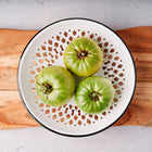 Three Aunt Ruby's German Green tomatoes in a decorative white bowl on a wooden cutting board.