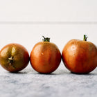 Three mahogany-colored Black Prince tomatoes with green shoulders lined up on a grey surface.