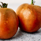 Two mahogany-colored Black Prince tomatoes with water droplets on a grey textured surface.