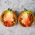 Two halves of a sliced Black Prince tomato showing mahogany flesh and seeds on a textured grey background.