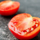 Two bright red Bonny Best tomato halves showing juicy, seeded interiors on a dark, textured surface.