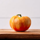 A single Hillbilly tomato with golden-yellow and red marbled skin, resting on a wooden cutting board.